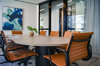 Stock image of a conference room, with orange leather chairs around a light wood table and an abstract blue painting on the wall.