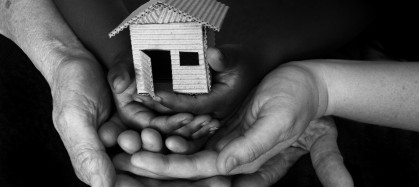 Three people's hands holding a miniature house