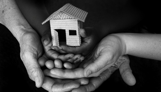 Three people's hands holding a miniature house