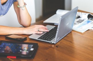 Image of woman sitting at a wooden desk using her computer, cell phone and tablet.