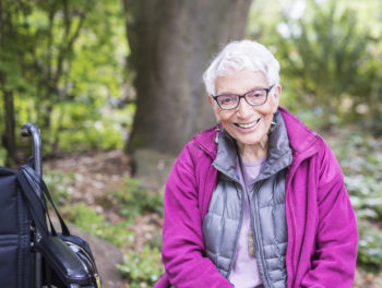 Older Woman Sitting in Park Beside her Wheelchair Happy and Smiling