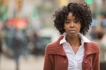 Young woman standing on city sidewalk with a somber gaze