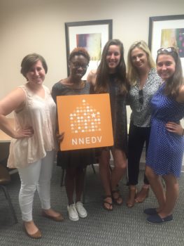 Photograph of NNEDV staff member Lysaundra Campbell, posing with summer 2016 interns in the office. They are holding an NNEDV sign.