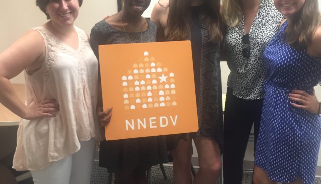Photograph of NNEDV staff member Lysaundra Campbell, posing with summer 2016 interns in the office. They are holding an NNEDV sign.